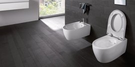 Ein modernes Badezimmer mit einem weißen WC und einem Bidet, beide auf einem eleganten, dunklen Boden platziert.