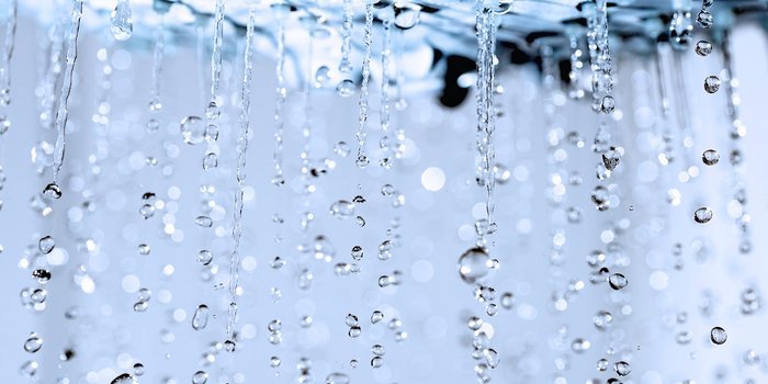 Wassertropfen fallen in einer sanften Bewegung, während sie im Licht funkeln und eine ruhige Atmosphäre schaffen.