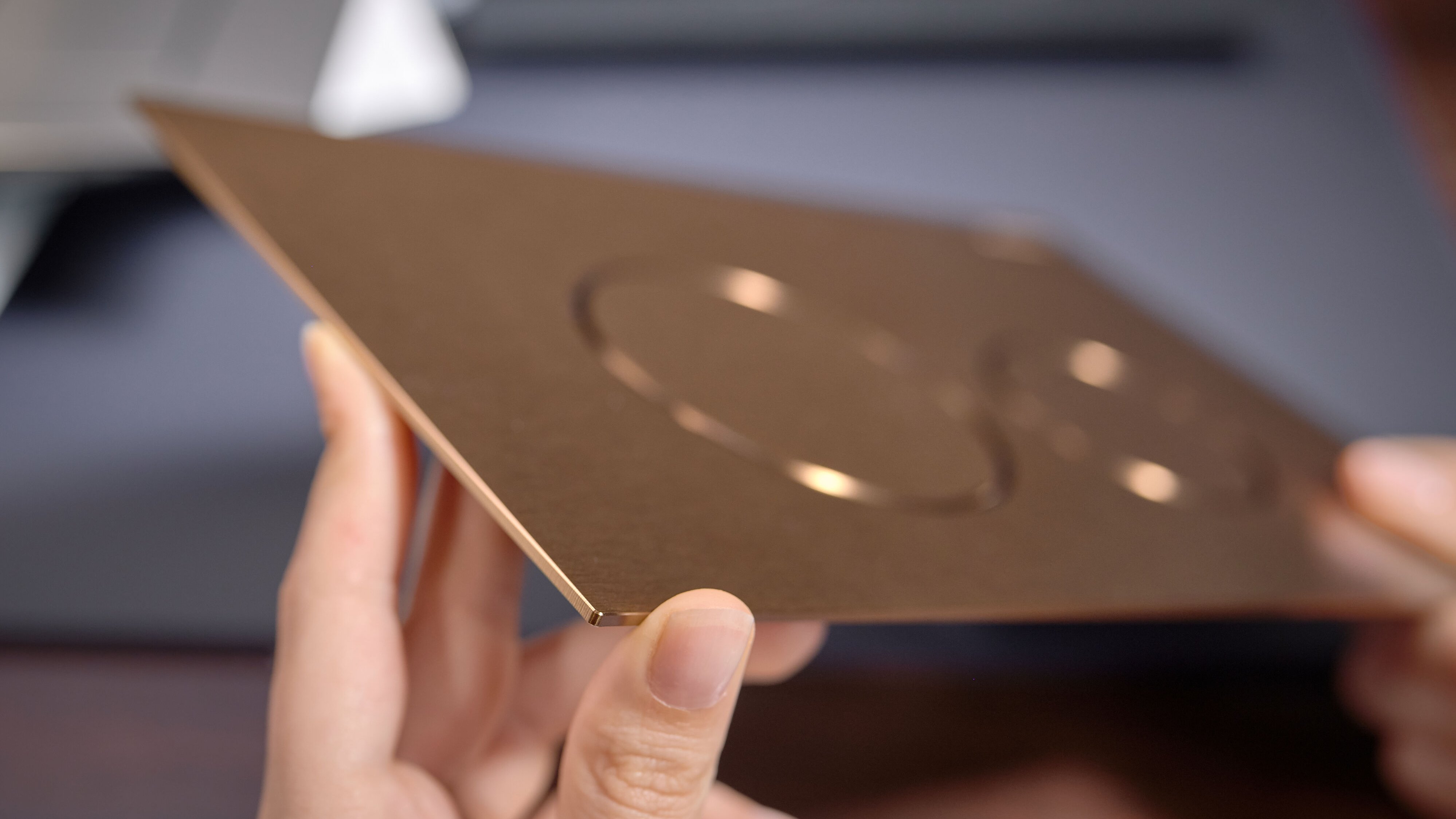 Eine Person hält ein glänzendes, goldfarbenes Blatt mit zwei runden Ausschnitten in der Mitte, auf einem Holztisch.