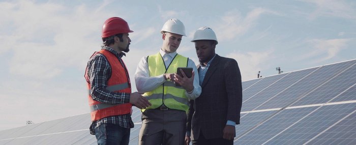 Drei Fachleute besprechen Solarenergie auf einem Feld Eine Photovoltaikanlage auf einer Wiese mit drei Männern die auf ein Tablet schauen