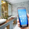 Moderne Badezimmeransicht mit Smartphone-Steuerung Ein modernes Badezimmer mit eleganten Waschbecken und einem Smartphone, das eine smarte Steuerung zeigt.